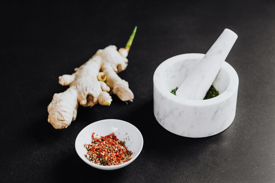 A culinary scene featuring a mortar with spices and ginger root on a black background.