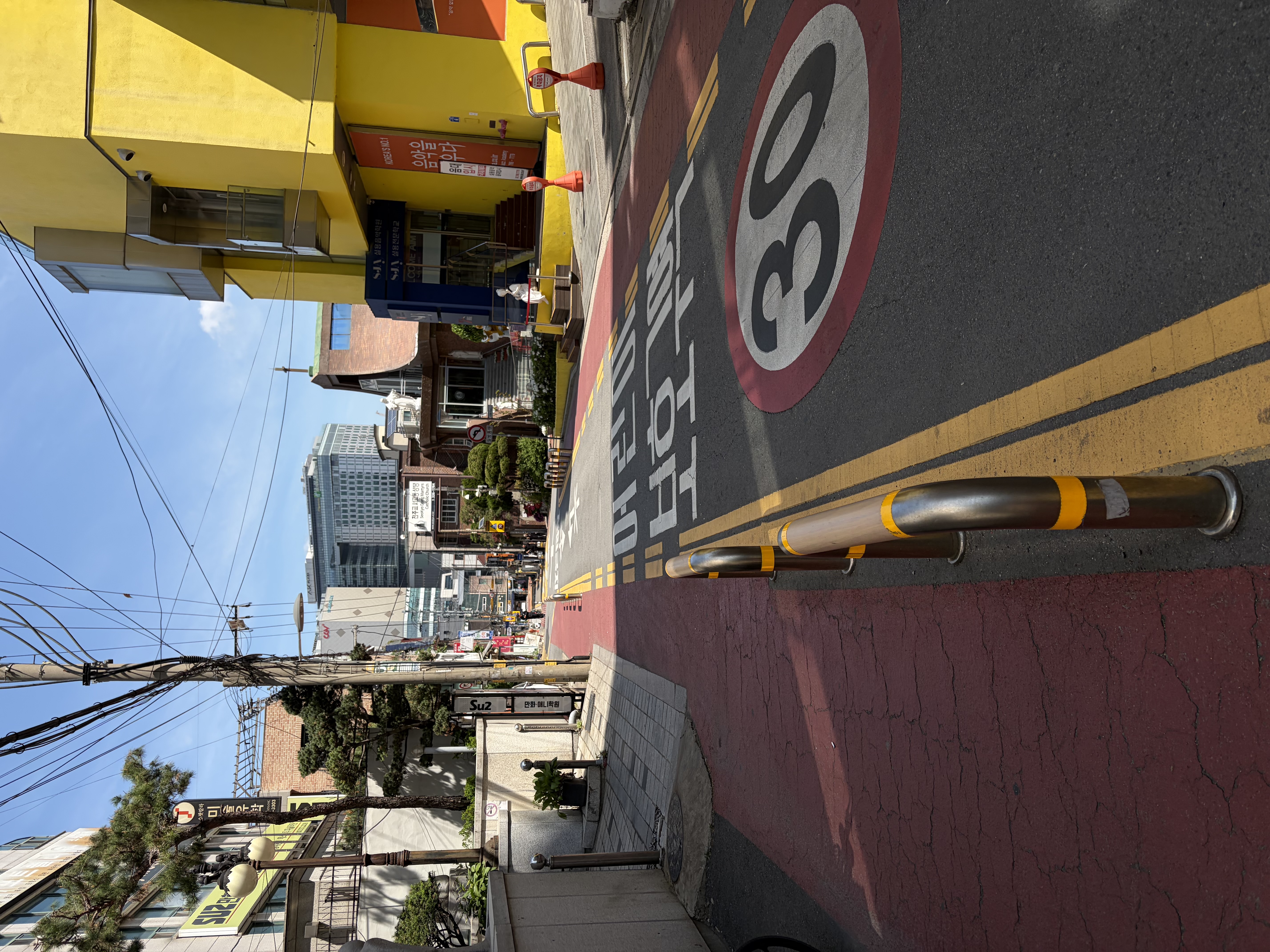 A sunny sloped street in Korea, with road markings and colorful buildings on both sides.