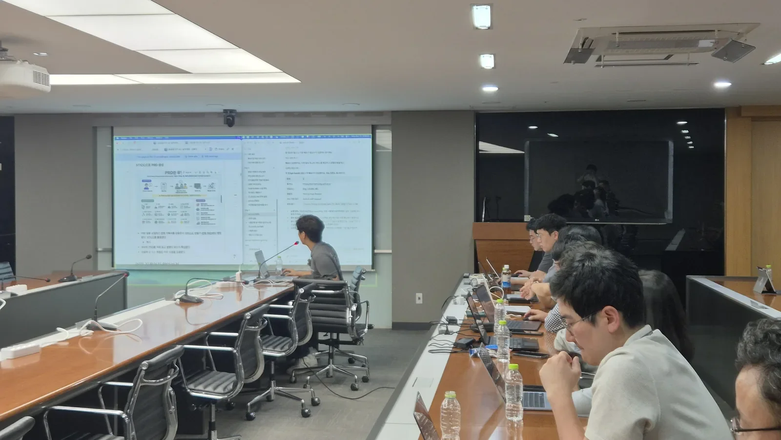 JB금융지주 교육 2회차, 스크린에 PRD 문서를 띄워 설명하고 임직원이 노트북으로 실습하는 모습